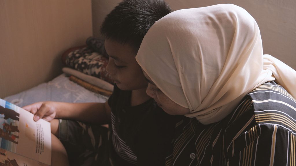svg+xml;charset=utf Collective for a Stronger Society Stories and Resources Mother with Son Reading a Book