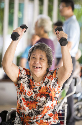 An elderly lady holding weights in the air