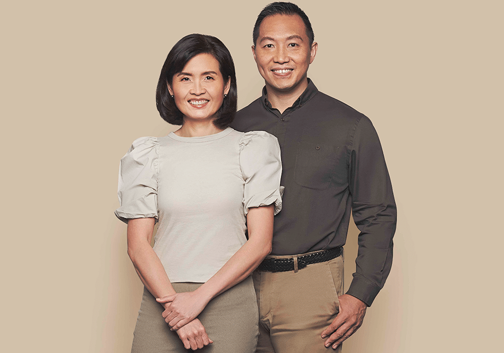 A man and woman posing for a photo against a beige background, capturing a joyful moment together.