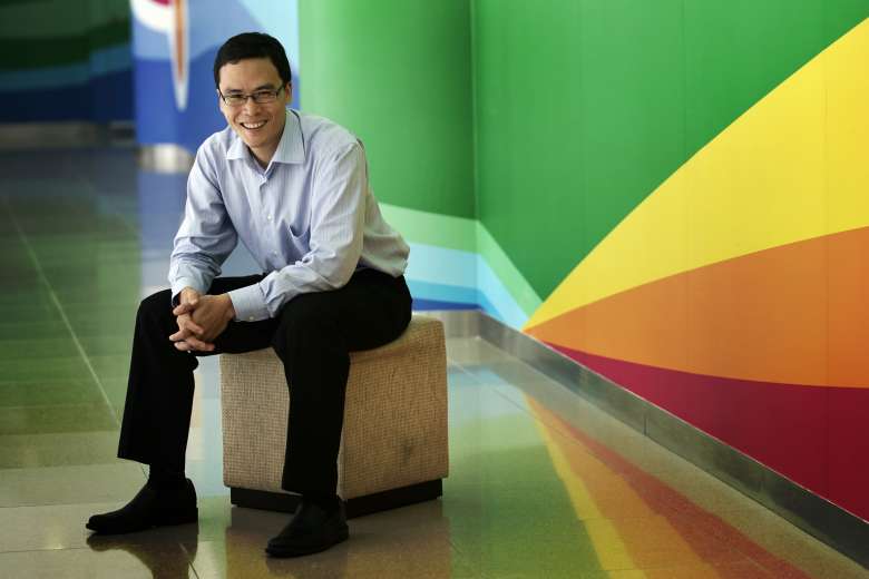 A man seated on a stool against a vibrant wall, exuding a lively ambiance.