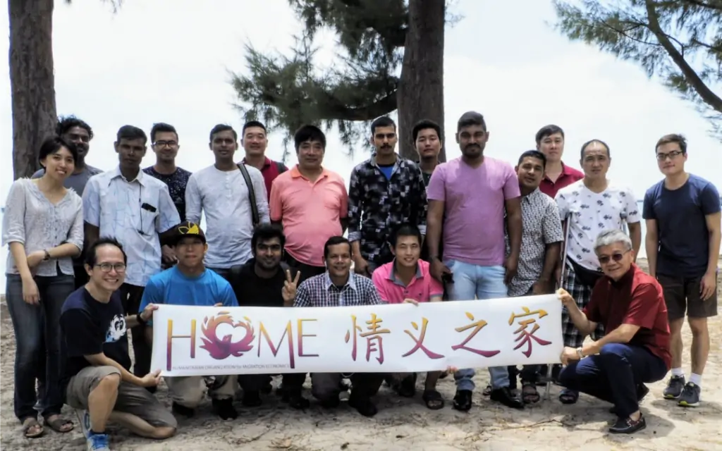 Happy group of individuals posing with a 'home' sign.