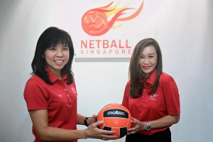 Two female individuals can be seen in the picture, both dressed in red shirts and holding a volleyball ball.