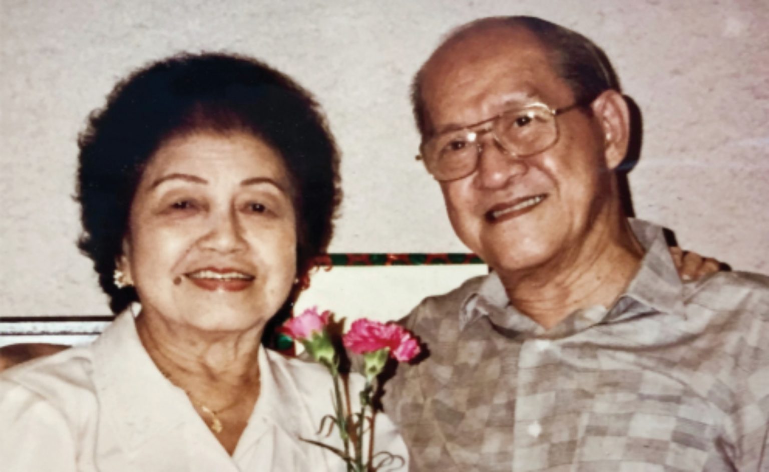 An older couple smiling while posing for a photo, holding a flower in their hands, radiating love and happiness.