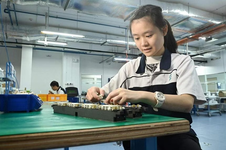 A woman diligently operating a computer amidst the bustling environment of a factory, focused on her tasks.