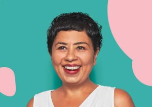 A woman with short hair and a white top smiling warmly, radiating positivity and joy.