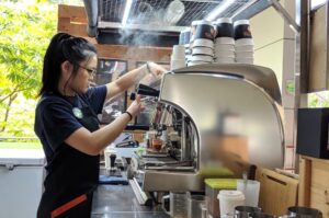 A woman expertly prepares coffee in a bustling coffee shop, showcasing her barista skills amidst the aromatic ambiance.