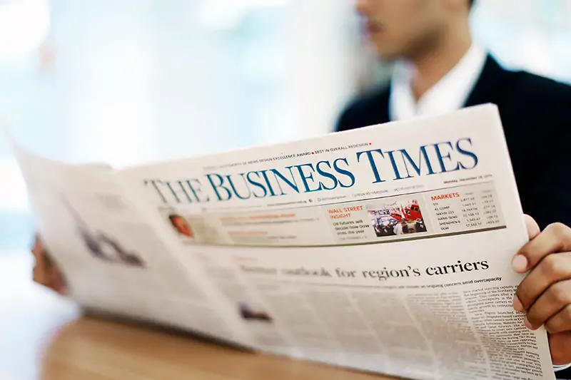 A professional man in a suit holds a newspaper displaying the Business Times, providing current business news.