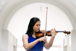 A woman gracefully plays the violin, showcasing her talent, dressed in a captivating blue gown.