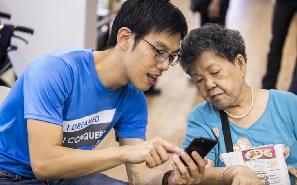 A younger Man teaching an woman how to use a smartphone.