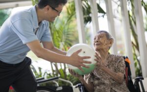 A man in a wheelchair kindly holds a ball for an elderly woman, showcasing compassion and support.