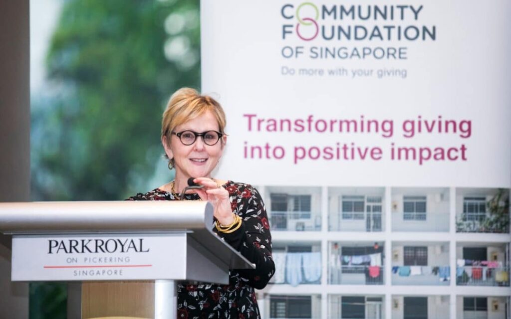 A woman confidently delivering a speech at a podium, standing before a sign, conveying her message with conviction and authority.