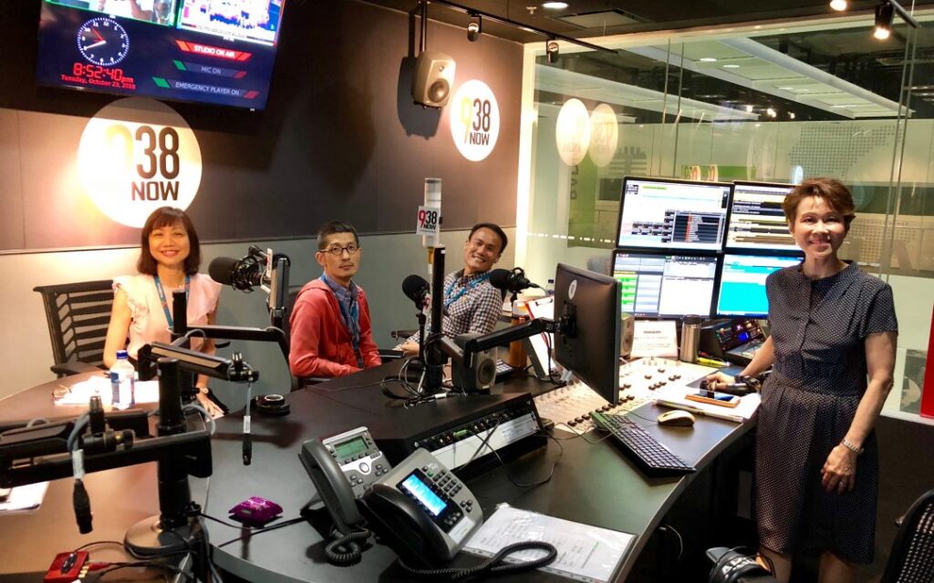 A group of people sitting at a desk with microphones and computers.