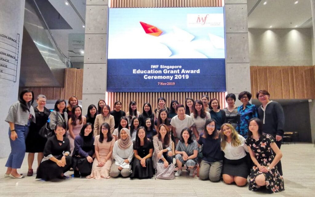 Women standing together for photo in front of big screen.