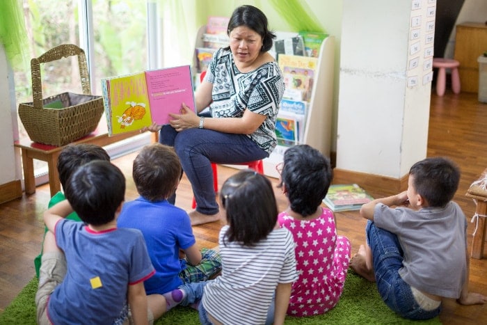 a teacher reading a story book to a group of kindergarteners