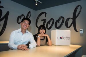 Two people seated at a table with a 'City of Good' sign in the background.