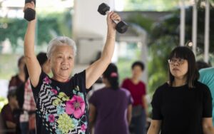 An image of a mature woman engaging in weightlifting exercises alongside a group of individuals.