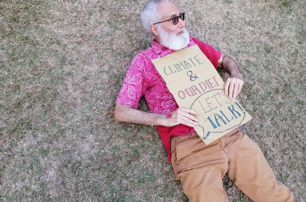 Elderly man lying on grass with sign.