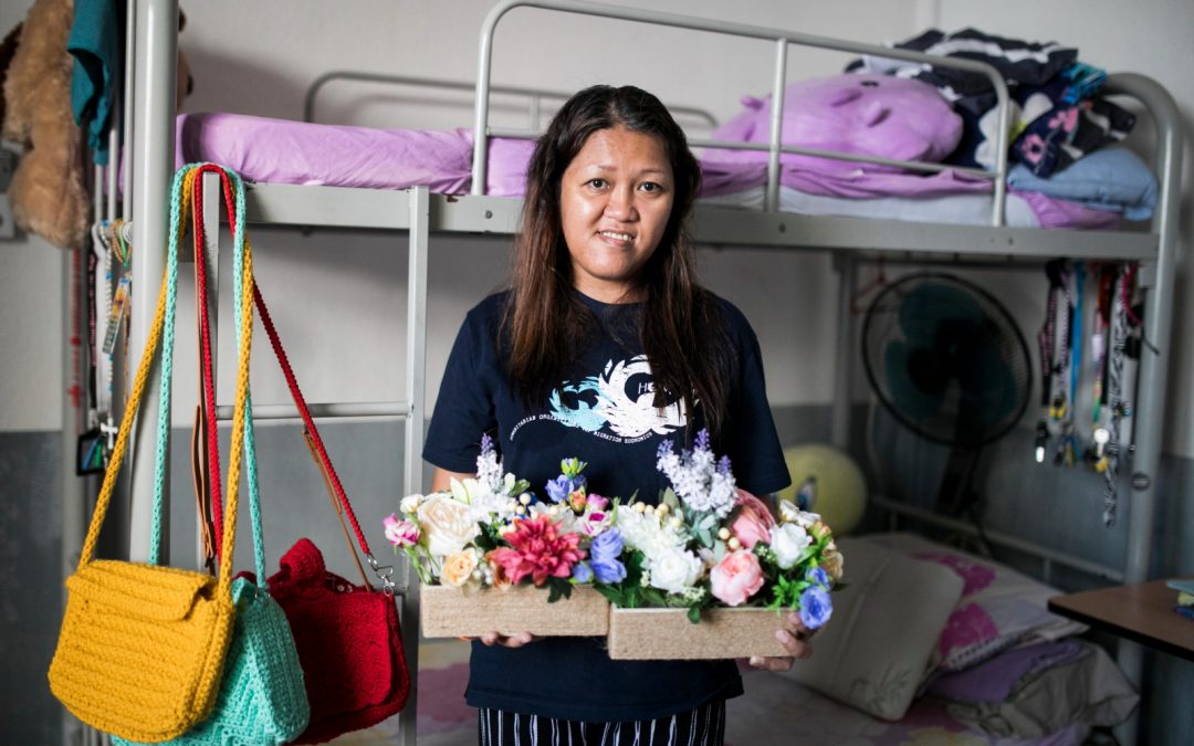 A woman gracefully holds a box of vibrant flowers, standing before a neatly arranged bunk bed.