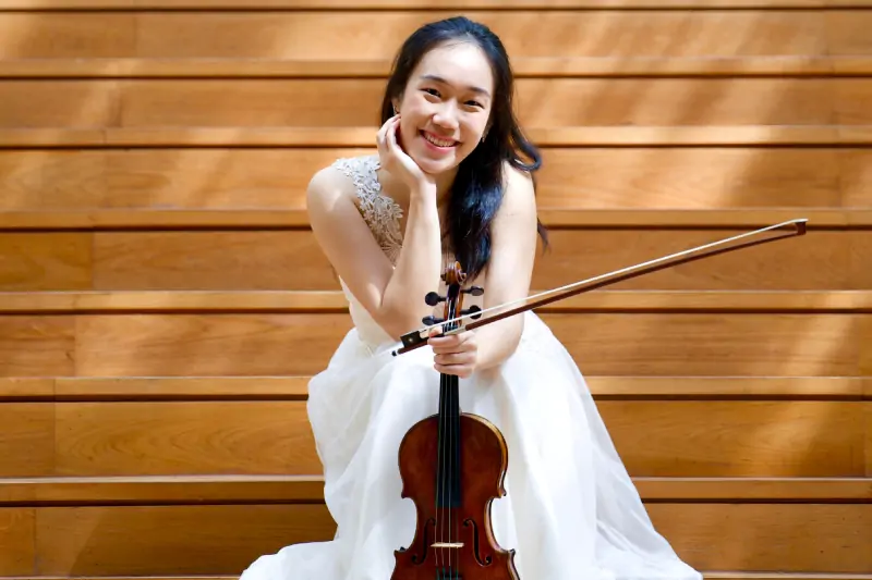 A woman in a white dress sits on stairs, gracefully holding a violin.